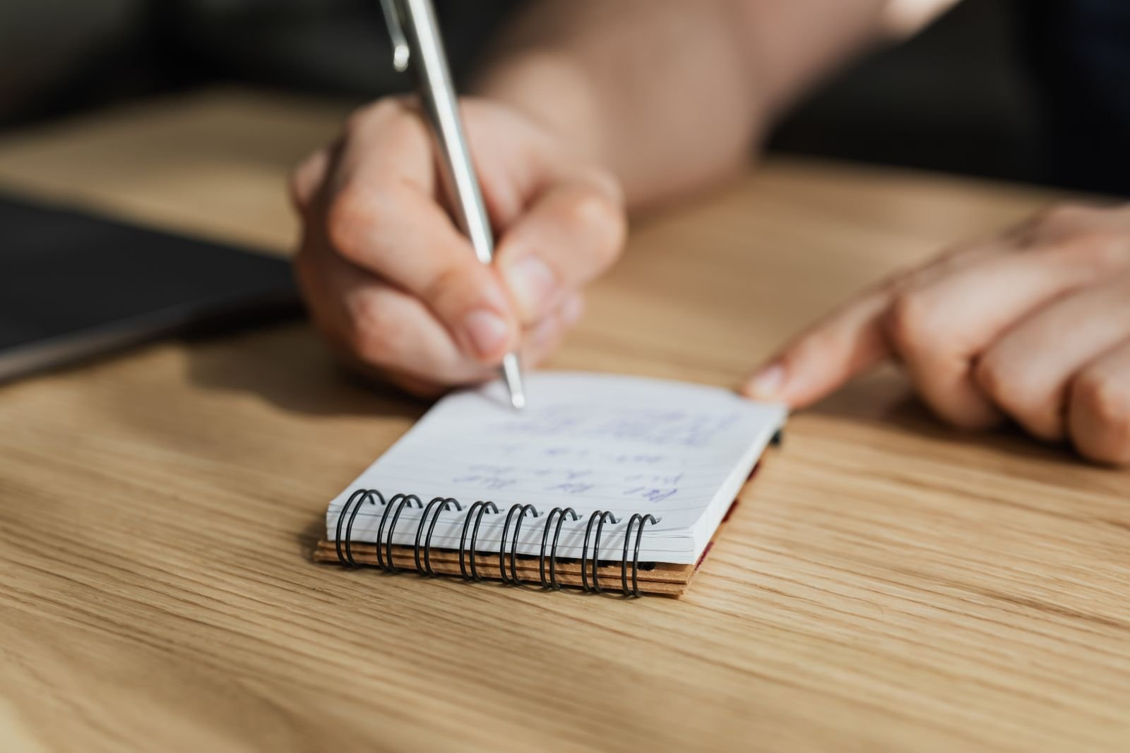 A hand writing careful notes in a small spiral notebook, the way a family documents a loss hour by hour